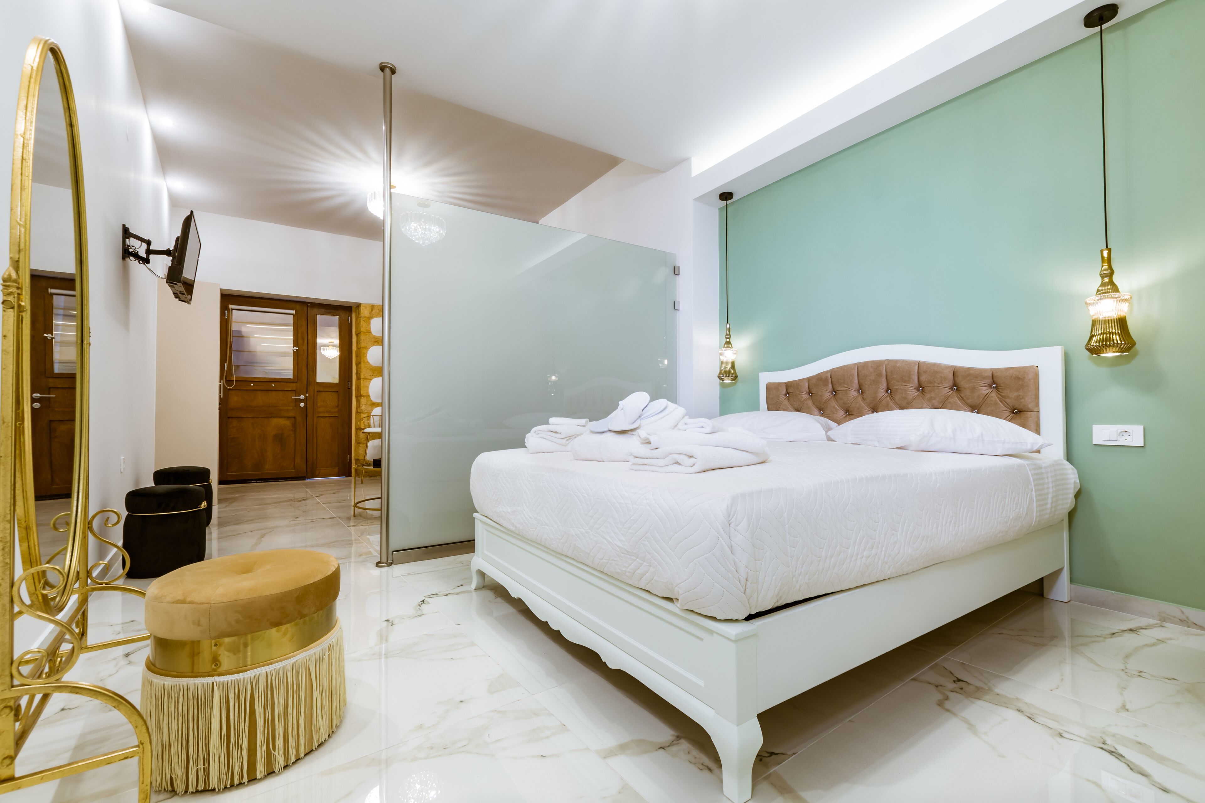 A bedroom with a white bed, a round ottoman, a large mirror, and a green wall.