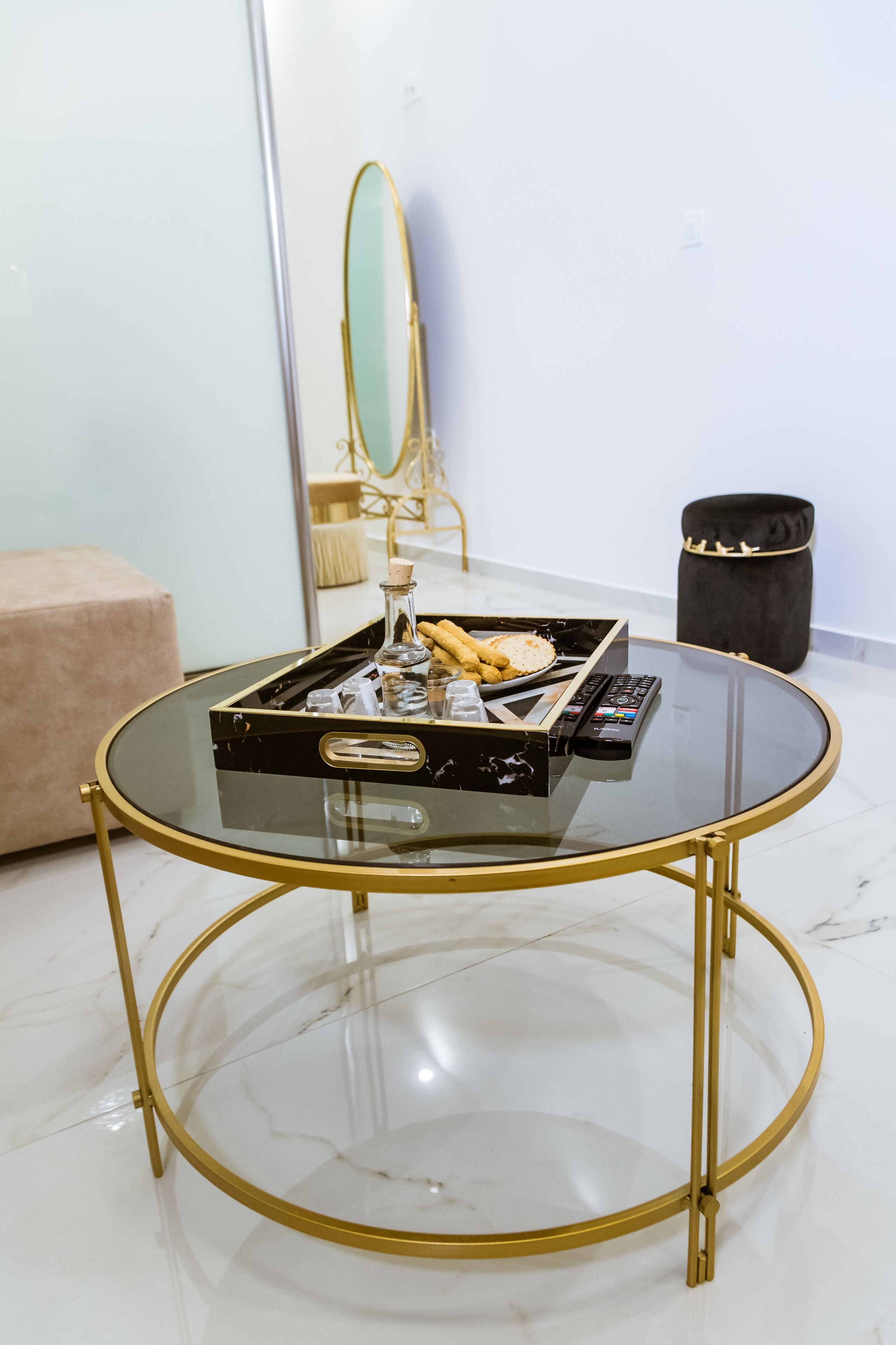 Une table ronde en verre avec un cadre doré, un plateau noir contenant divers objets, et un miroir en arrière-plan.