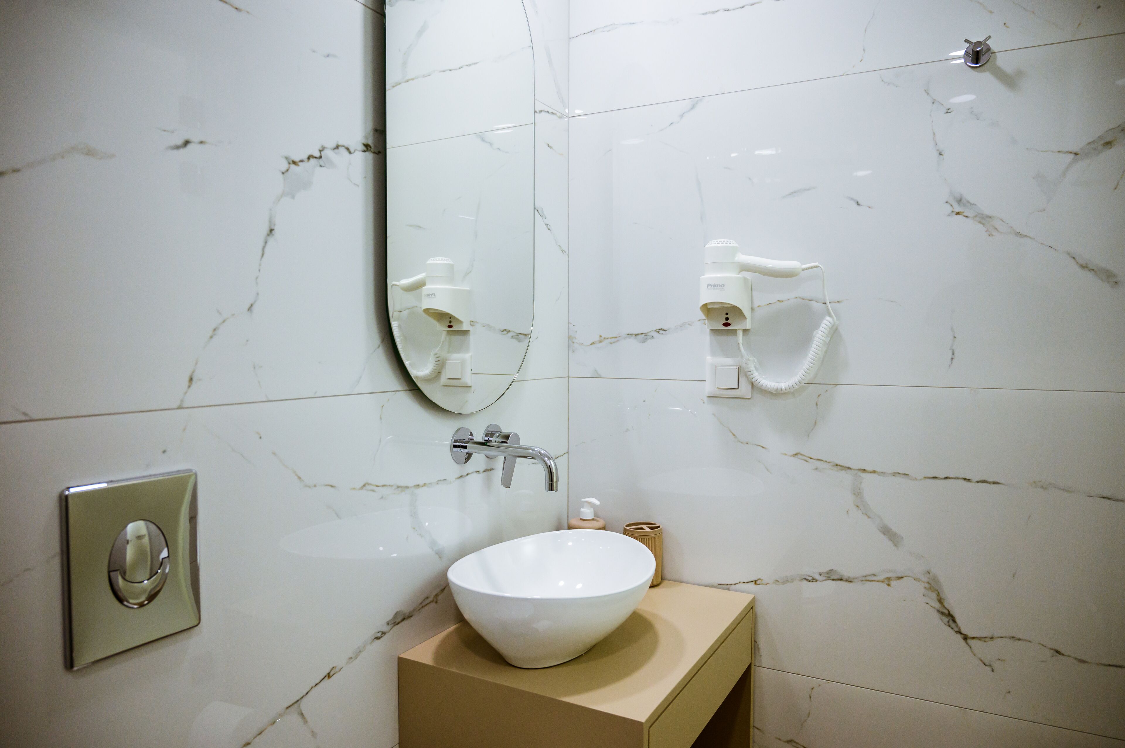 Casa de banho com lavatório de mármore branco, espelho, dispensador de toalhas e dispensador de sabonete.