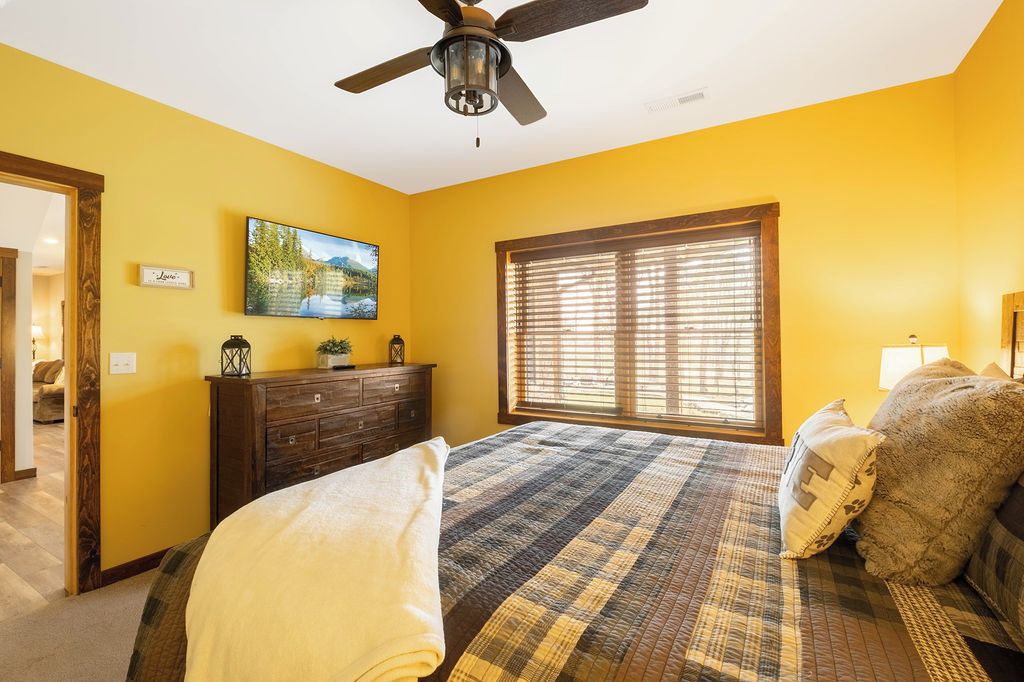 A bedroom with a bed, a ceiling fan, a window with blinds, a dresser, and a painting on the wall.