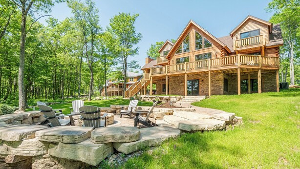 Ein großes Blockhaus mit Steinunterbau, mehreren Terrassen und einer Sitzgelegenheit im Freien mit Adirondack-Stühlen.