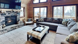 Ein gemütliches Wohnzimmer mit Kamin aus Stein, einem großen Fenster, einer Couch und einem Couchtisch.