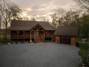 A log cabin with a porch, a covered garage, and a gravel driveway. - A Lil Slice of Heaven by Taylor Made Deep Creek (McHenry)