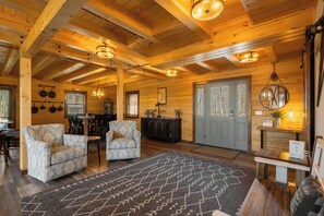 A cozy log cabin interior with a dining area, two armchairs, a patterned rug, and a wooden ceiling. - A Lil Slice of Heaven by Taylor Made Deep Creek (McHenry)