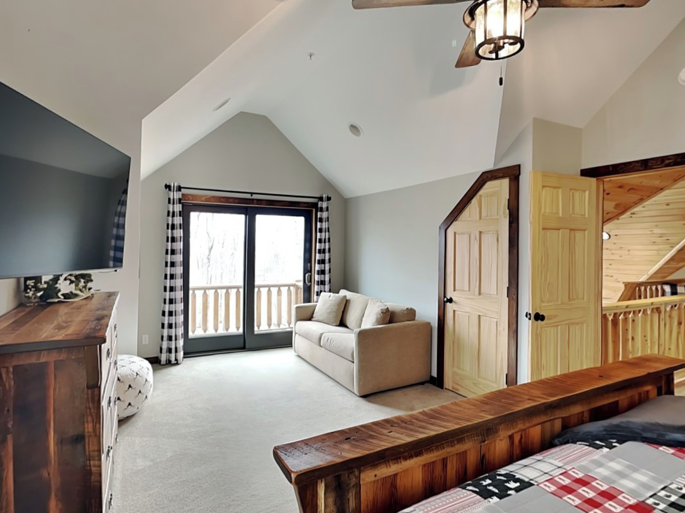 A bedroom with a sloped ceiling, a wooden bench, a sofa, and a door leading to a staircase.