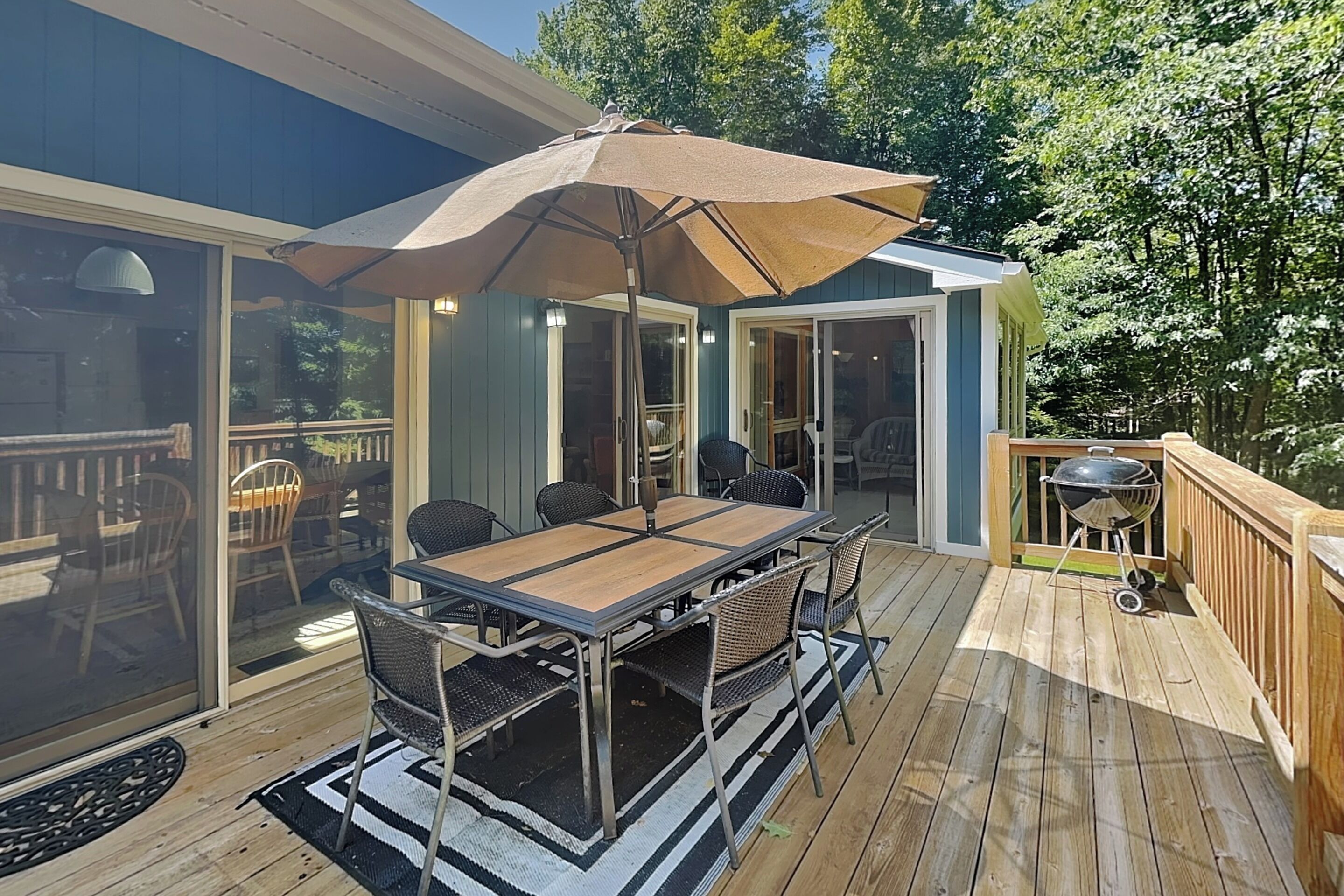 An outdoor patio with a table and chairs, a large umbrella, and a grill.