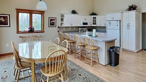 Une cuisine moderne avec des meubles blancs, un îlot central et un coin repas doté de chaises en bois.