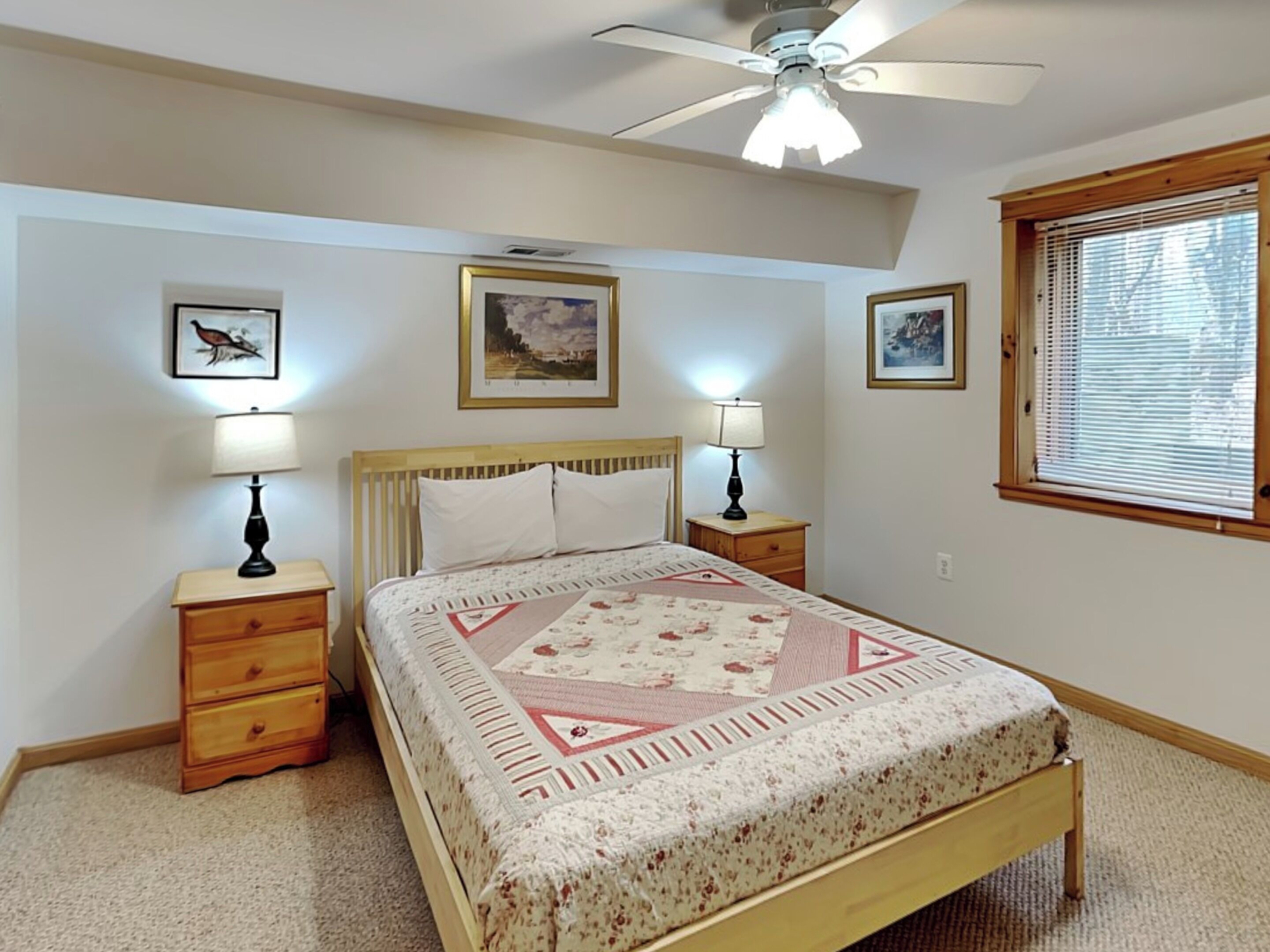 A bedroom with a bed, two bedside tables, a ceiling fan, and framed pictures on the wall.