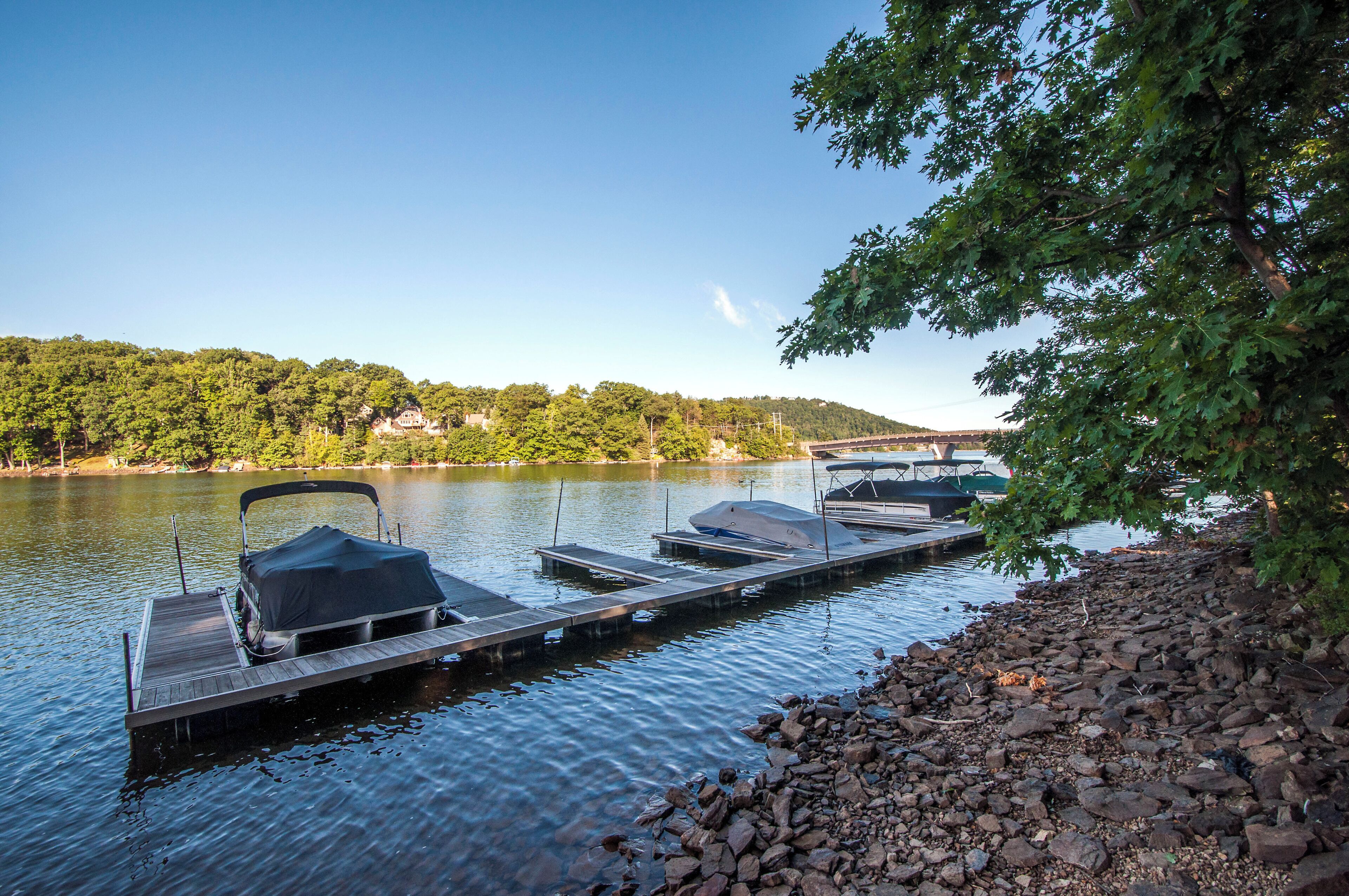 A dock with covered boats, a rocky shoreline, and a forested hill in the background.
