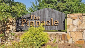 Une enseigne en bois portant l’inscription « The Pinnacle », placée devant un mur de pierres, et entourée de verdure.