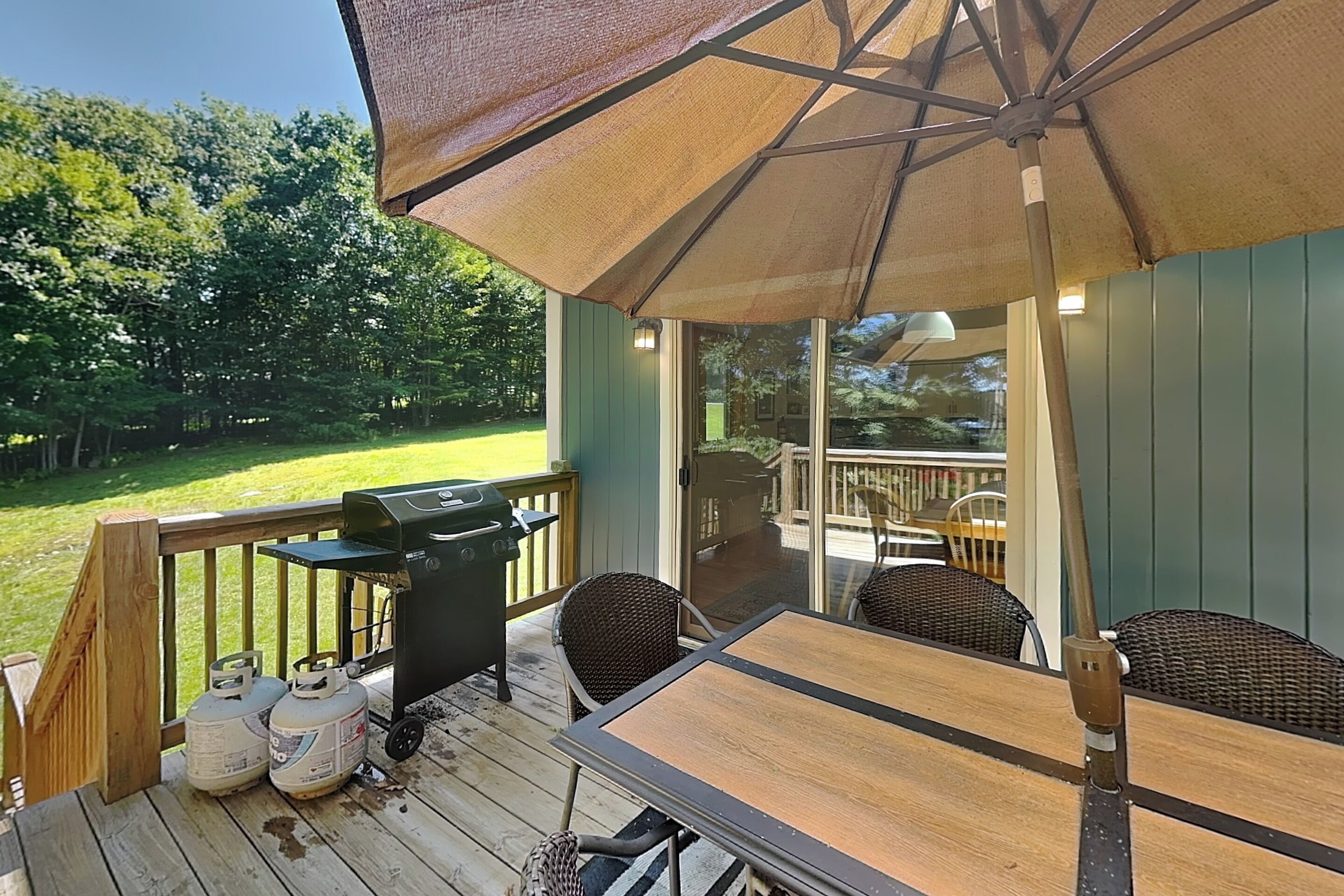 A covered outdoor deck with a table and chairs, a grill, and propane tanks.