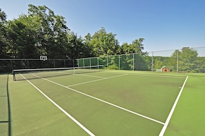 Una cancha de tenis con una red, rodeada por una valla y árboles.