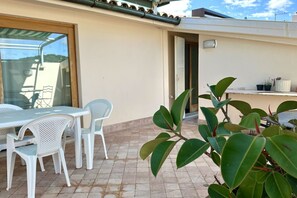 En terrasse med et bord, stole, en glasdør og en potteplante.