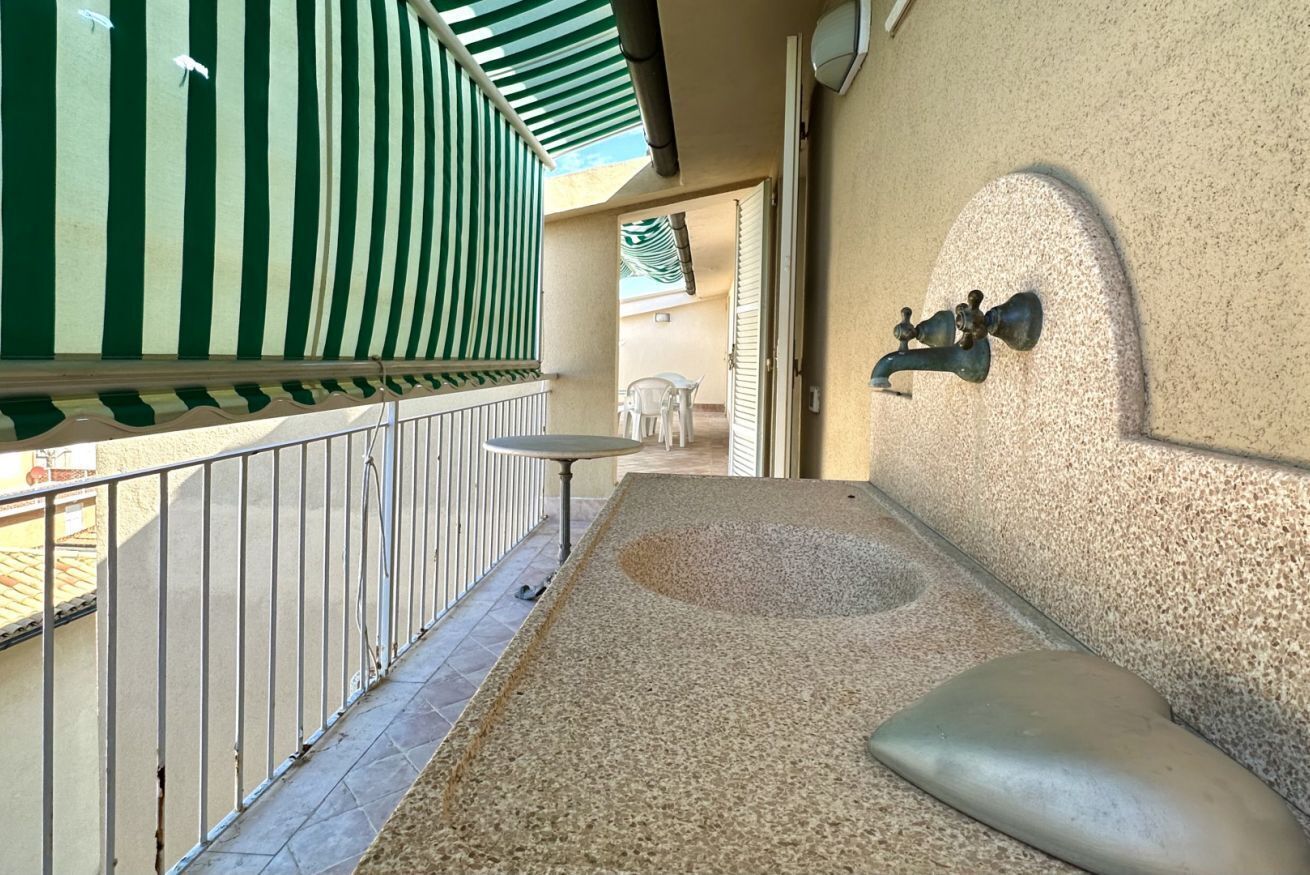 Un balcone con un tenda a righe verdi, un tavolino e un lavabo fissato alla parete.