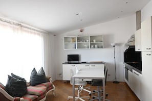 A compact living space with a sofa, a dining table, a TV, and kitchen appliances.