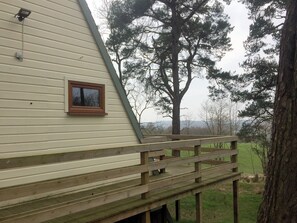 Une terrasse en bois avec une rambarde, une fenêtre et une vue sur un arbre et le paysage.