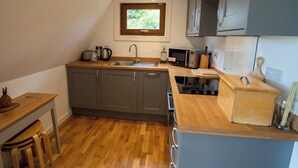 Cocina pequeña con armarios grises, encimera de madera, microondas integrado y una ventana sobre el fregadero.