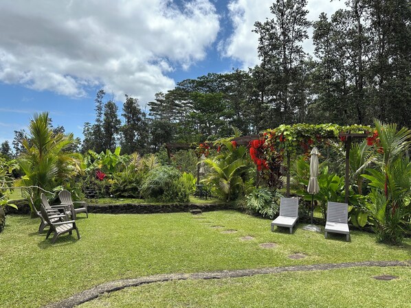Un jardin bien entretenu, avec une pelouse, deux chaises longues et une pergola ornée de fleurs rouges.