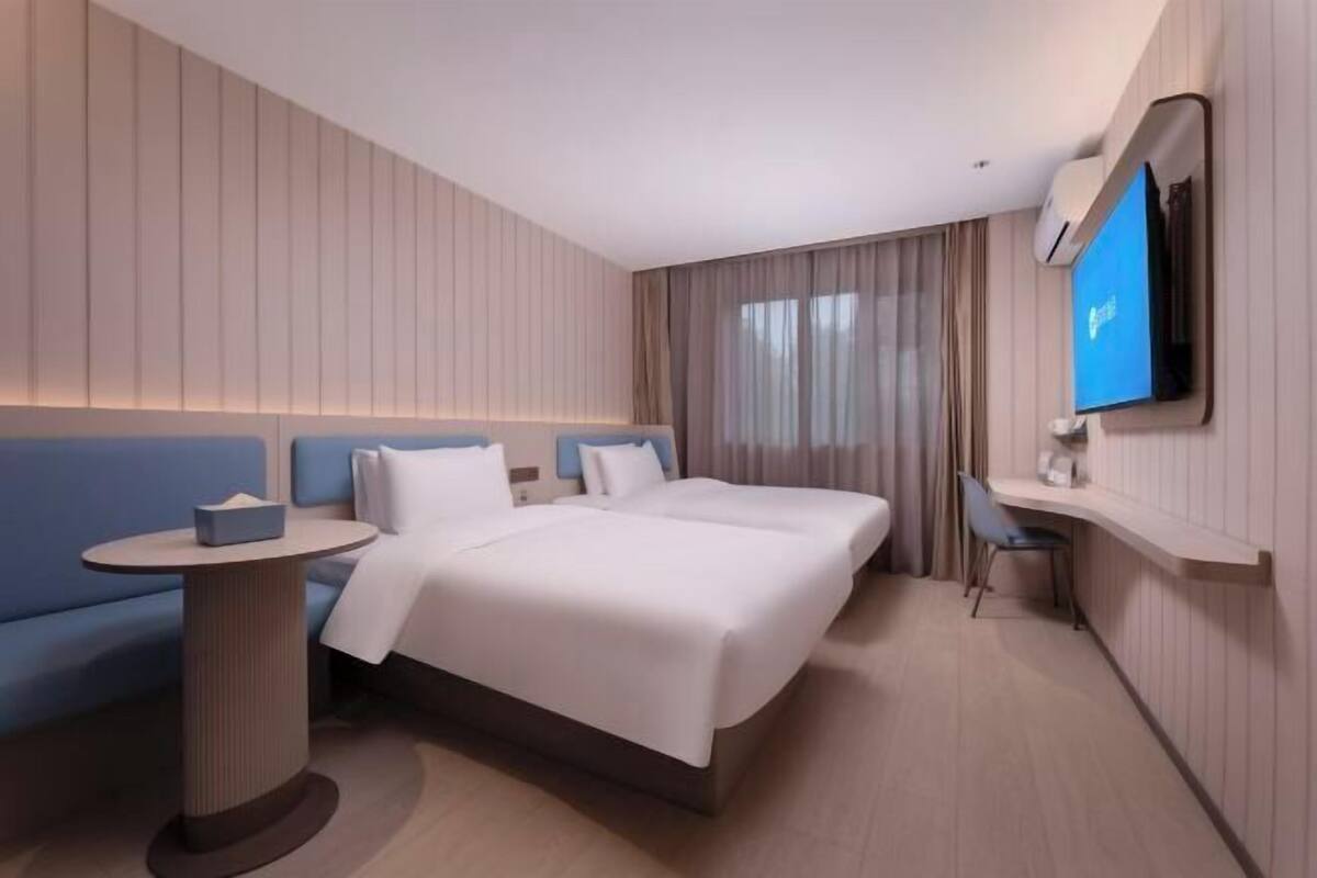 Une chambre d’hôtel avec un grand lit, une petite table ronde, un canapé bleu, un téléviseur fixé au mur et un bureau avec une chaise.
