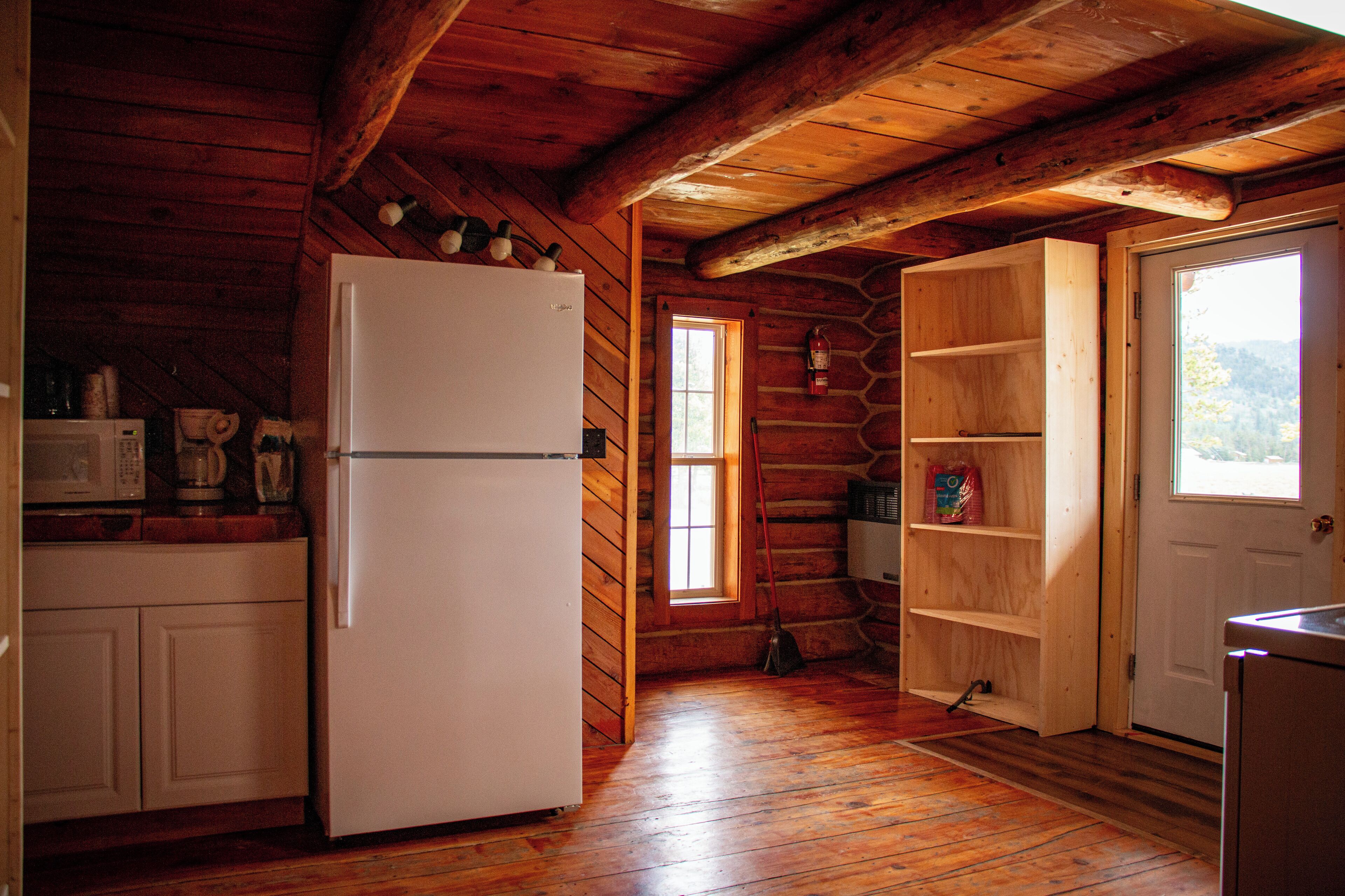 Cocina de cabaña de madera con un refrigerador, estantes de madera y una ventana.