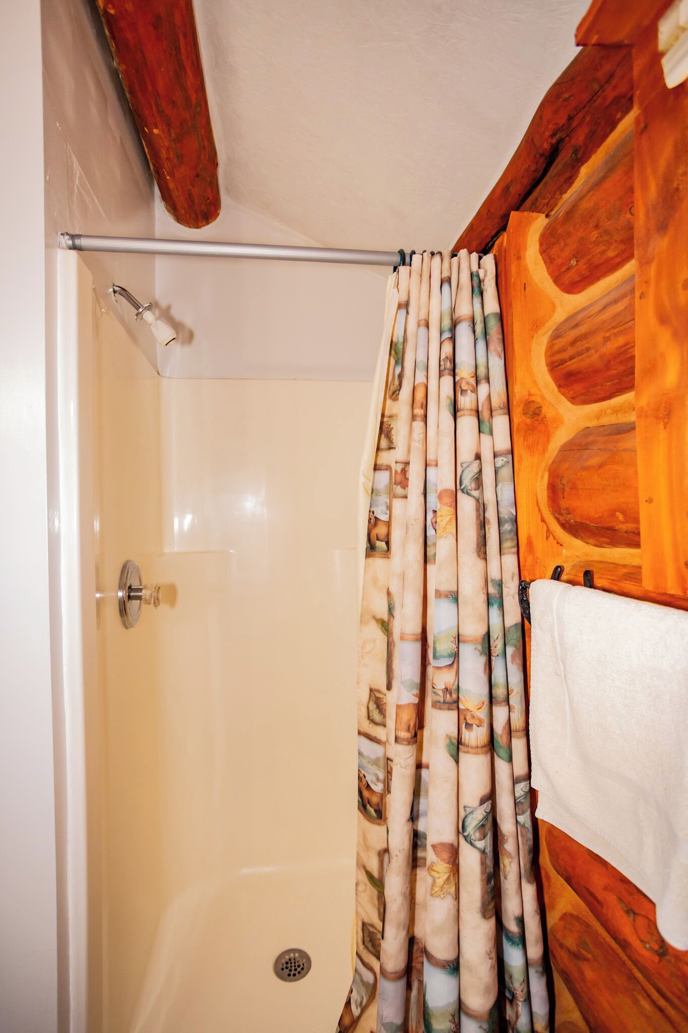 Une douche avec un rideau de douche à motifs de bambou, un panneau mural en bois et une tringle de douche en métal.