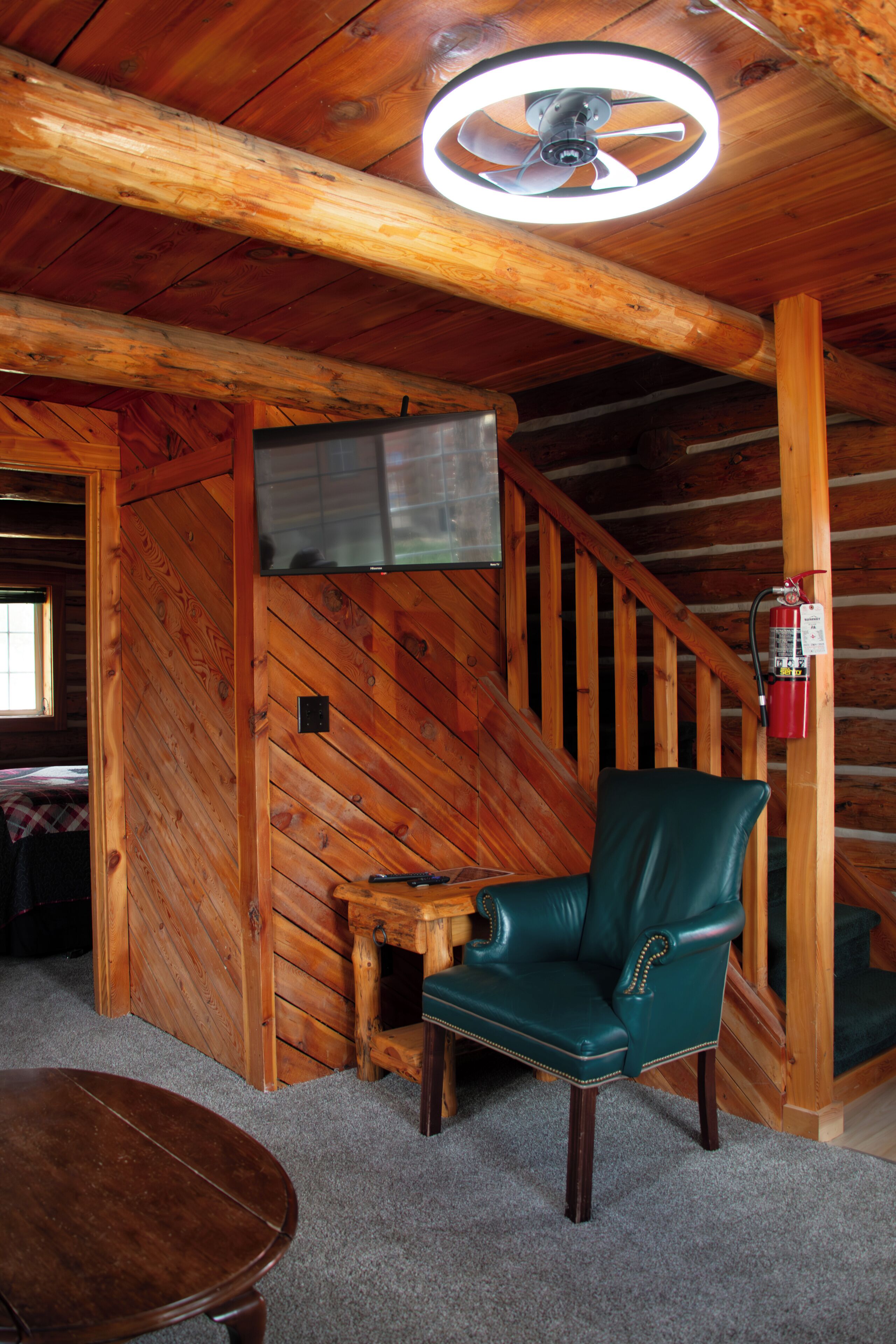 Un interior de madera con una silla de cuero verde, una mesa de madera y una escalera.