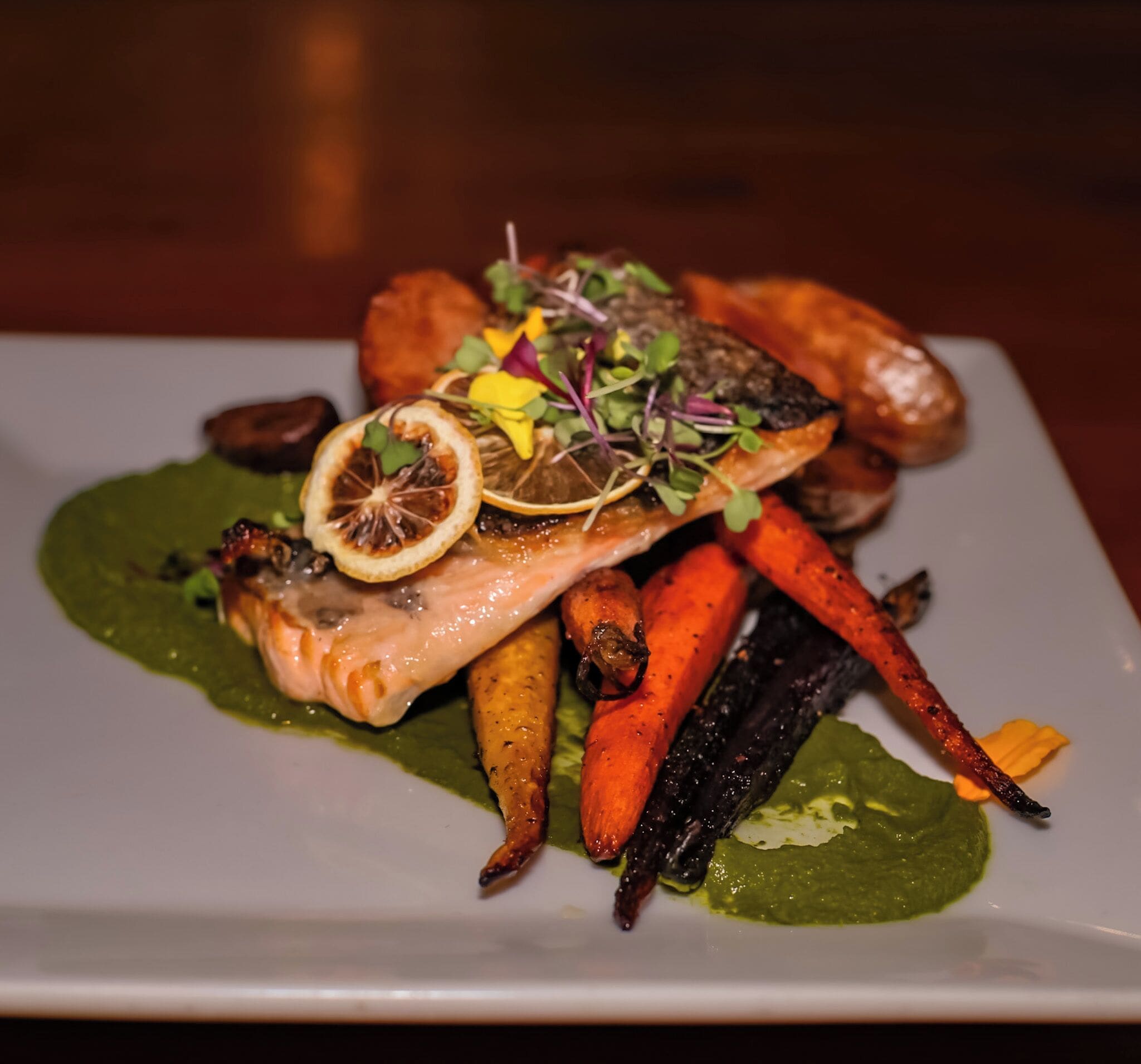 A plate of food with salmon, carrots, and greens.