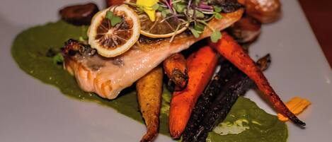 A plate of food with salmon, carrots, and greens.