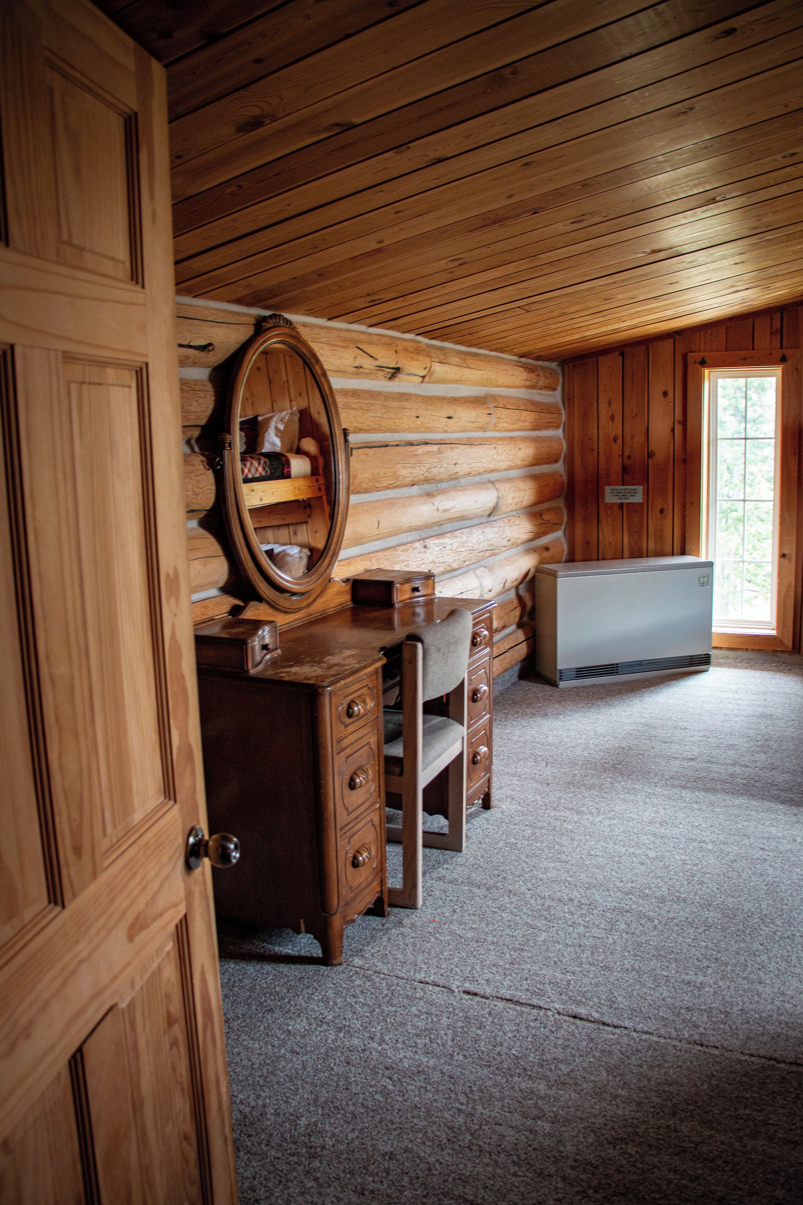 Une chambre aménagée dans un chalet en rondins, avec une commode en bois, un miroir et un chauffage intégré.