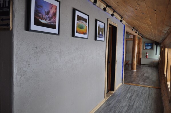 A hallway with framed pictures on the wall, wooden beams on the ceiling, and a wooden floor.