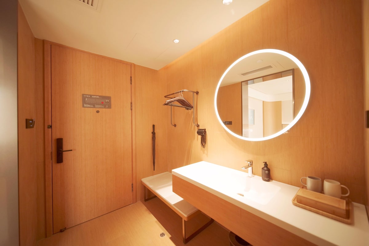 A modern bathroom with a wooden vanity, a round mirror with a light, and a towel rack.