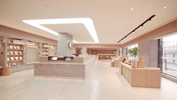 A modern hotel lobby with a reception desk, seating area, and large windows.