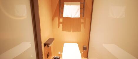 Une petite salle de bain comprenant des toilettes, une poubelle, un porte-serviettes avec une serviette et une petite étagère.