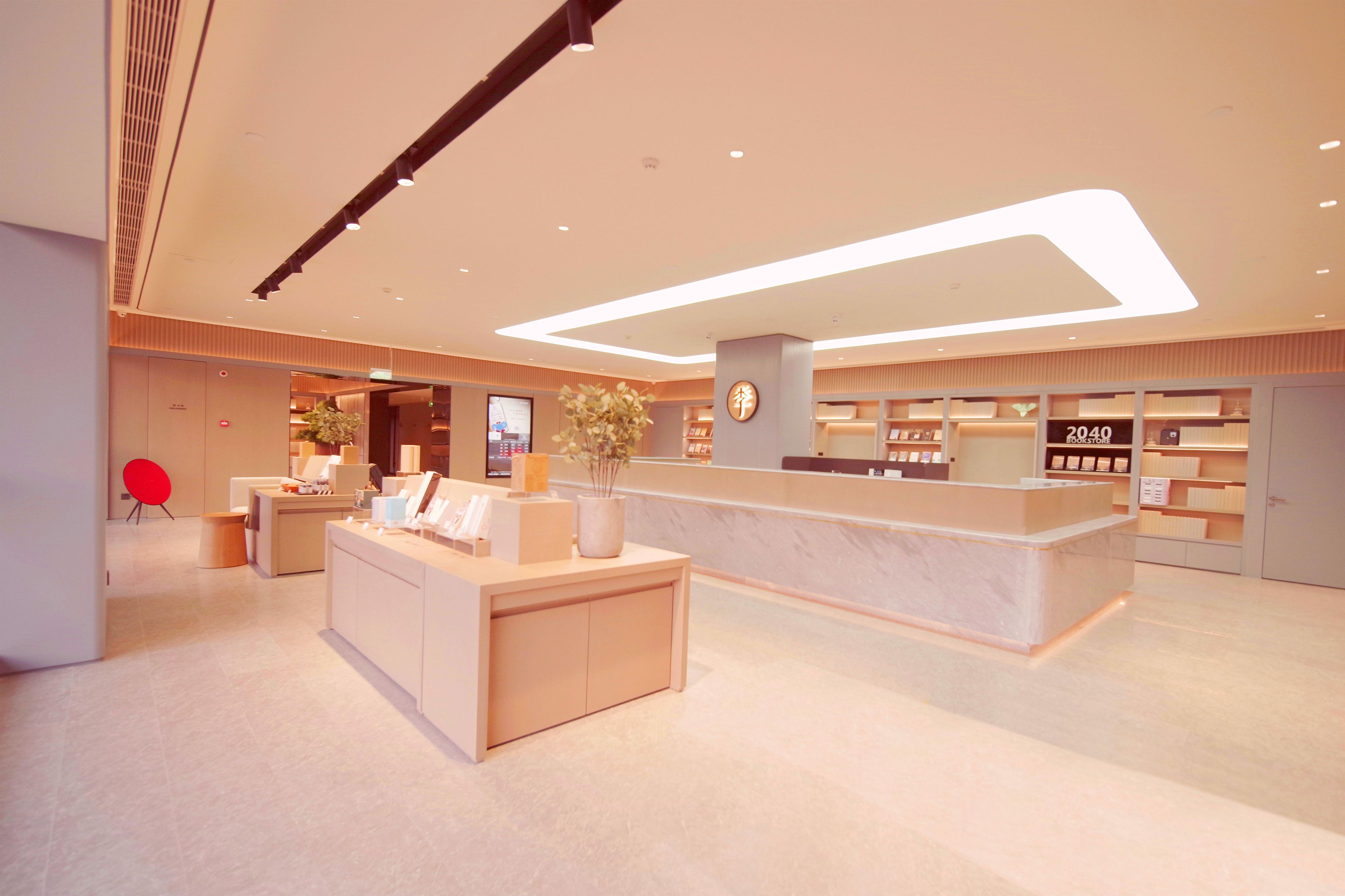 A modern hotel lobby with a reception desk, a digital information screen, and a bookstore.