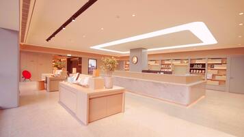 A modern hotel lobby with a reception desk, a digital information screen, and a bookstore.