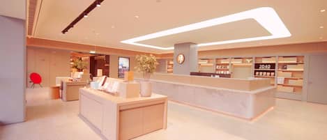 A modern hotel lobby with a reception desk, a digital information screen, and a bookstore.