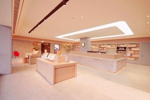 Un hall d’hôtel moderne comprenant un comptoir d’accueil, un écran d’information numérique et une librairie.