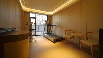 A modern gym with a treadmill, chairs, and a desk.