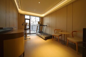 A modern gym with a treadmill, chairs, and a desk. - Ji Hotel (Beijing)