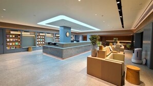 A modern hotel lobby with a reception desk, seating area, and a bookshelf filled with books. - Ji Hotel (Beijing)