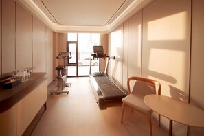 A hotel room with a treadmill, a desk with water bottles, a chair, and a table. - Ji Hotel (Beijing)