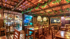 A restaurant with wooden tables and chairs, hanging lights, and a view of the bar area. - Hotel & Spa El Escondite de la Montaña (Sabana Redonda)