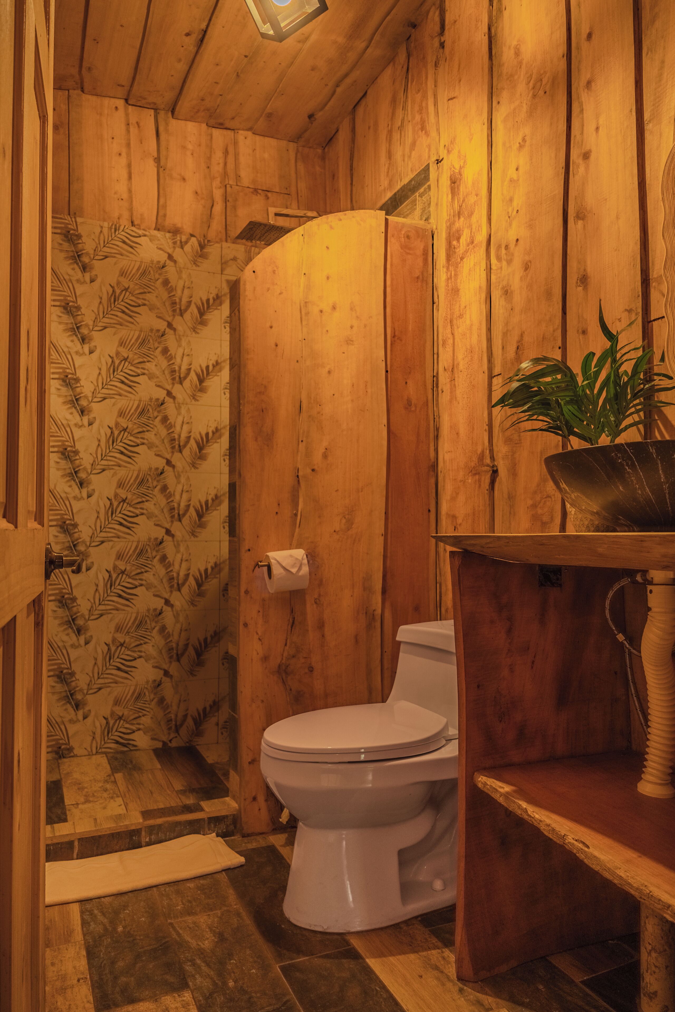 A wooden bathroom with a toilet, a sink, and a shower.