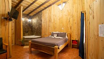 A wooden cabin room with a bed, a stone wall, a stone fireplace, a wooden ceiling, and a mounted television.