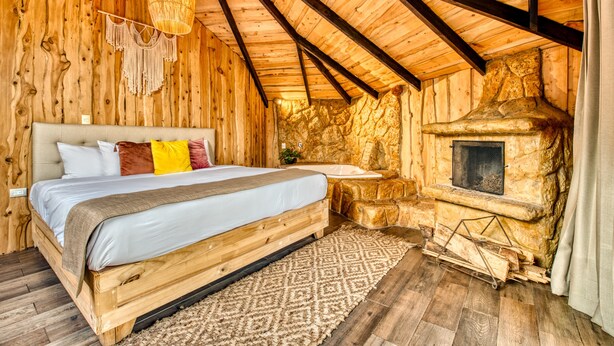 A wooden cabin bedroom with a bed, a stone fireplace, and a hanging light fixture. - Hotel & Spa El Escondite de la Montaña (Sabana Redonda)