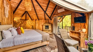 A wooden cabin with a bed, a fireplace, a TV, and a balcony with wicker furniture. - Hotel & Spa El Escondite de la Montaña (Sabana Redonda)