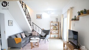 Ett modernt vardagsrum med en grå soffa, ett träbord, en tv på ett träställ och en trappa med ett svart räcke.