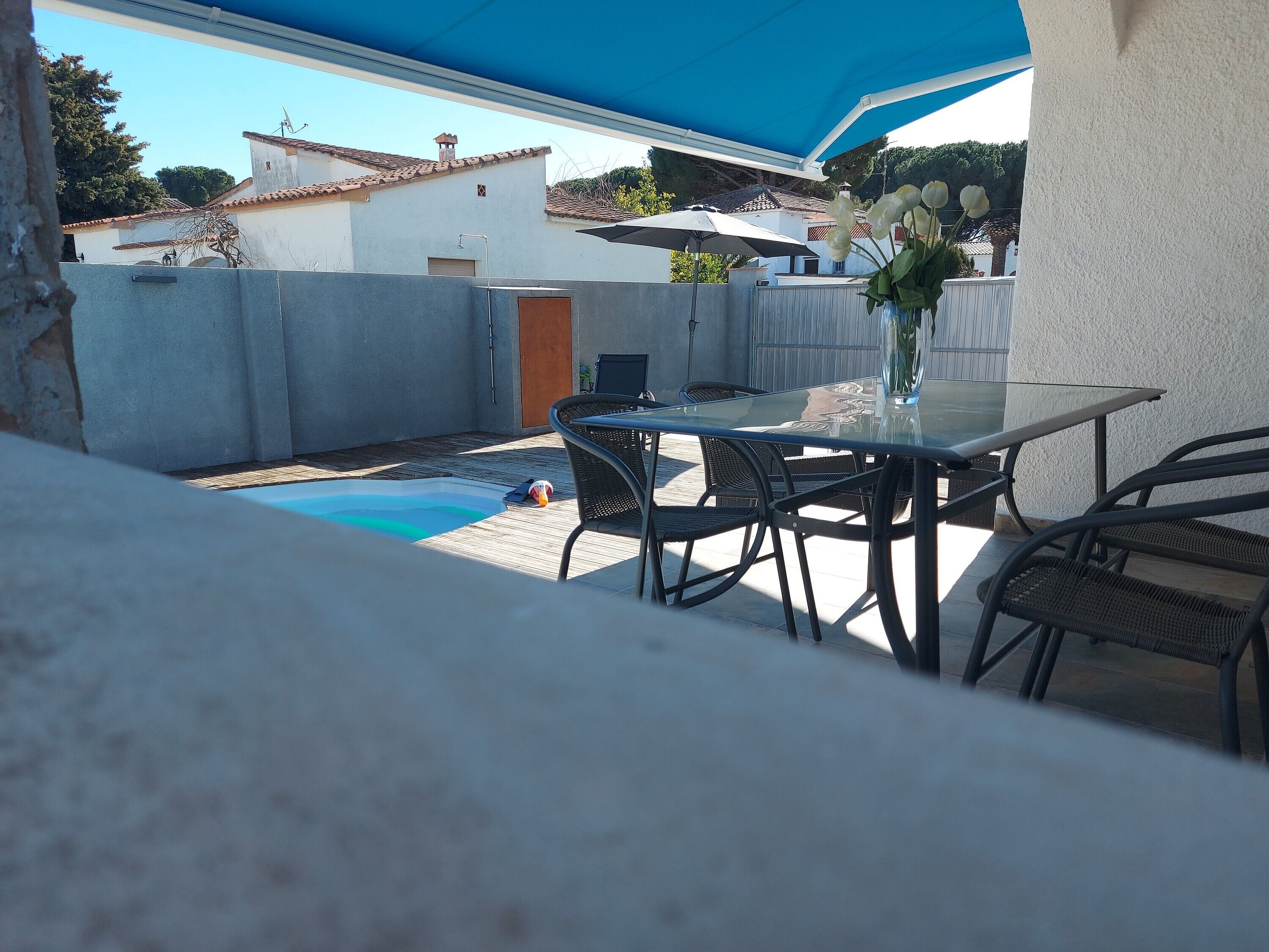 Eine Terrasse mit Glastisch und -stühlen, einem kleinen Pool und einem blauen Sonnensegel.
