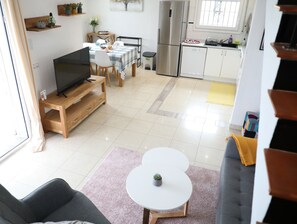 A modern living room with a TV, sofa, and coffee table. A kitchen with a fridge and stove is visible in the background. - Villa 3 bedrooms, 2 bathrooms, private pool, air conditioning and wifi (L'Escala)
