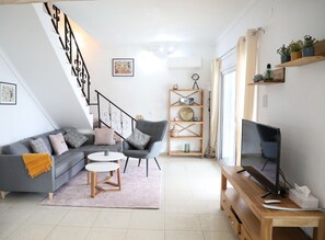 A modern living room with a grey sofa, a wooden coffee table, a TV on a wooden stand, and a staircase with a black railing. - Villa 3 bedrooms, 2 bathrooms, private pool, air conditioning and wifi (L'Escala)